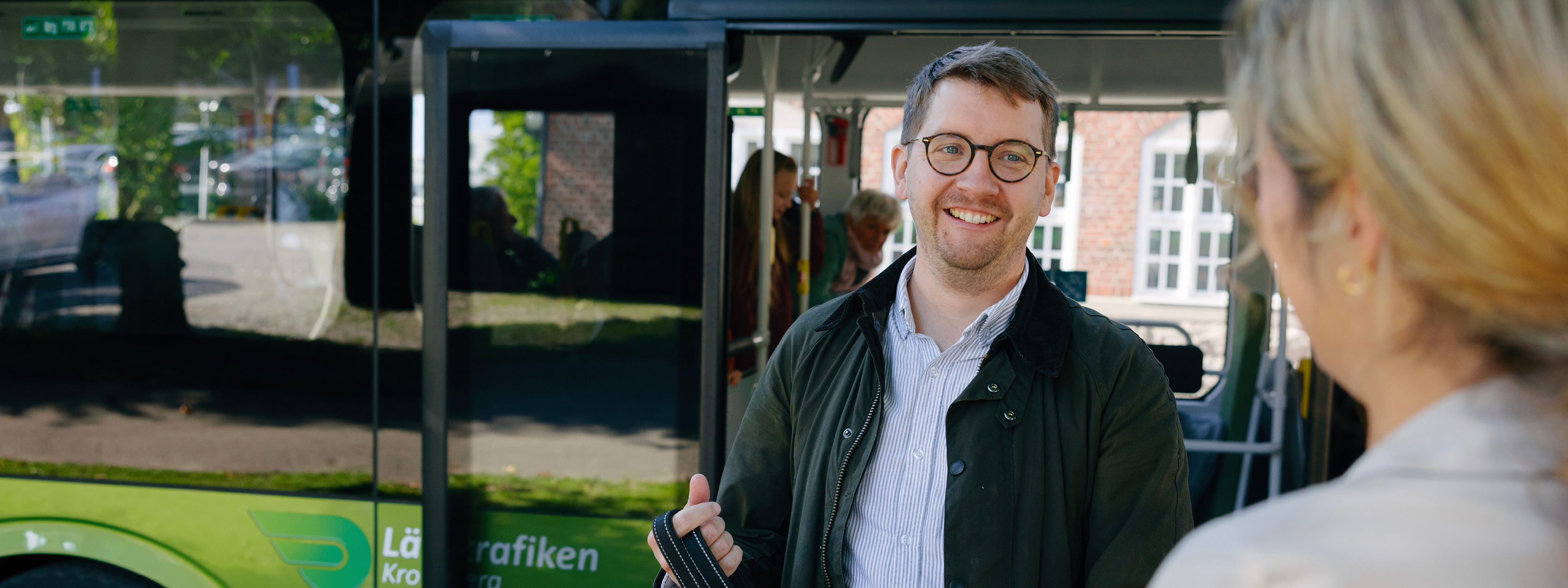 Man står med ryggen mot en buss. Mannen bär glasögon och en grön jacka.
