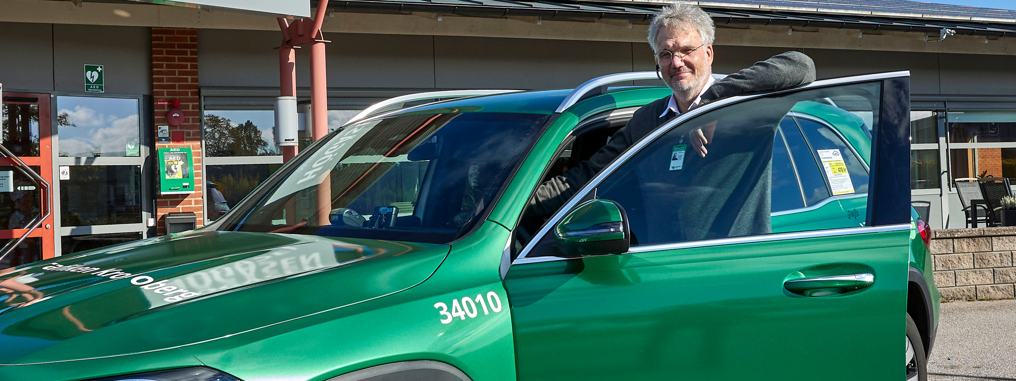 En man står vid en grön bil. Mannen hänger lite lätt på framdörren.