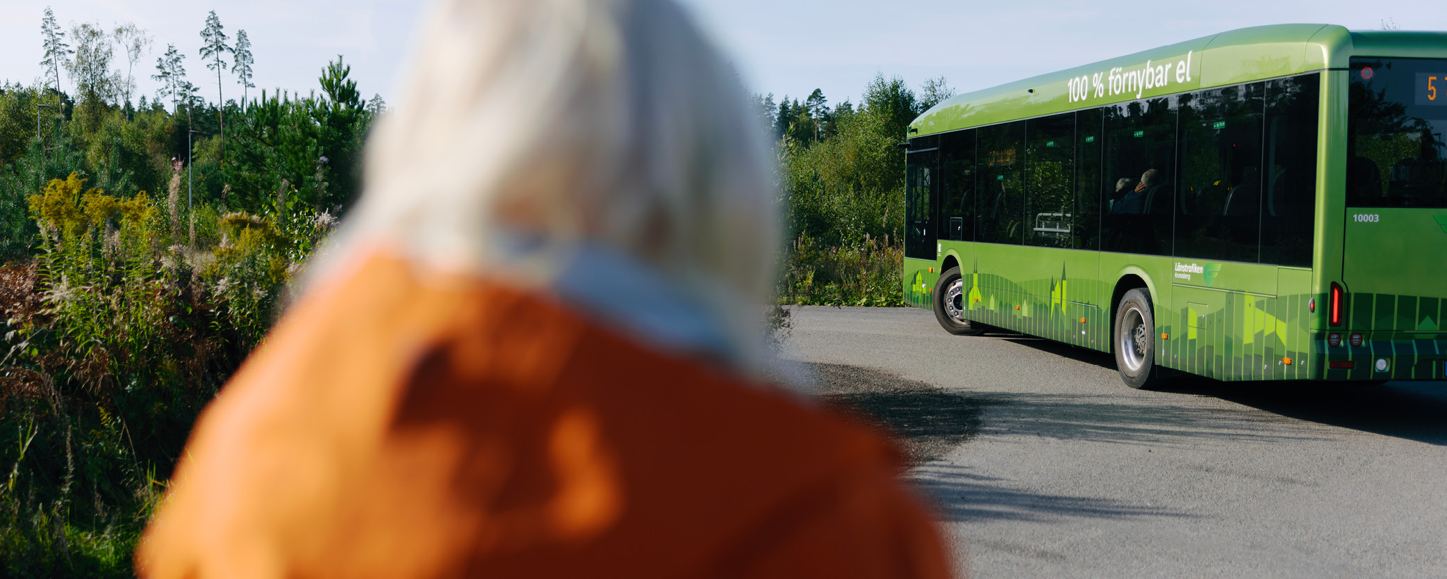 Kvinna står vid sidan av en buss. Bussen är i fokus.