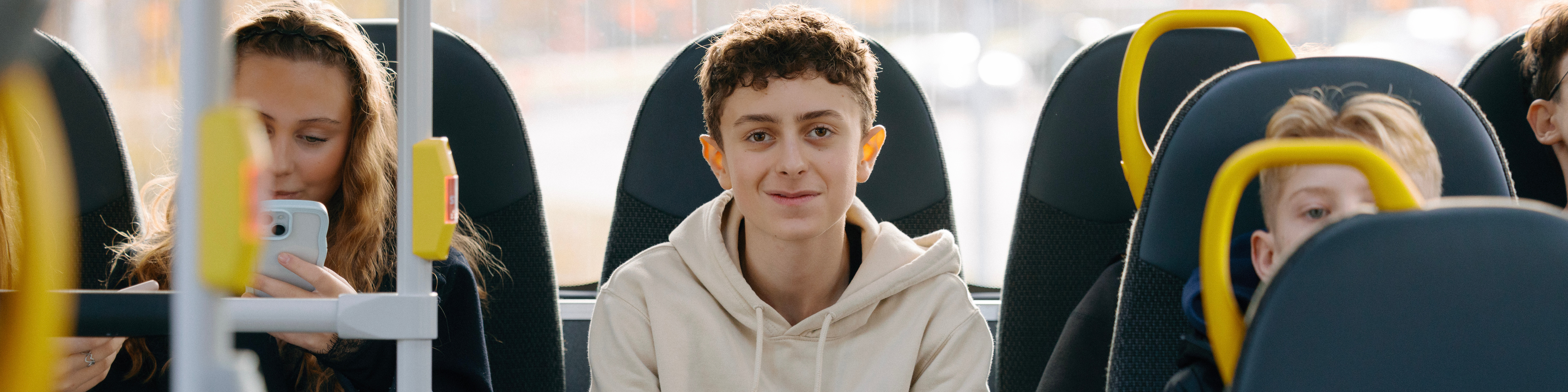 En kille sitter längst bak i bussen. Han ler in i kameran. 