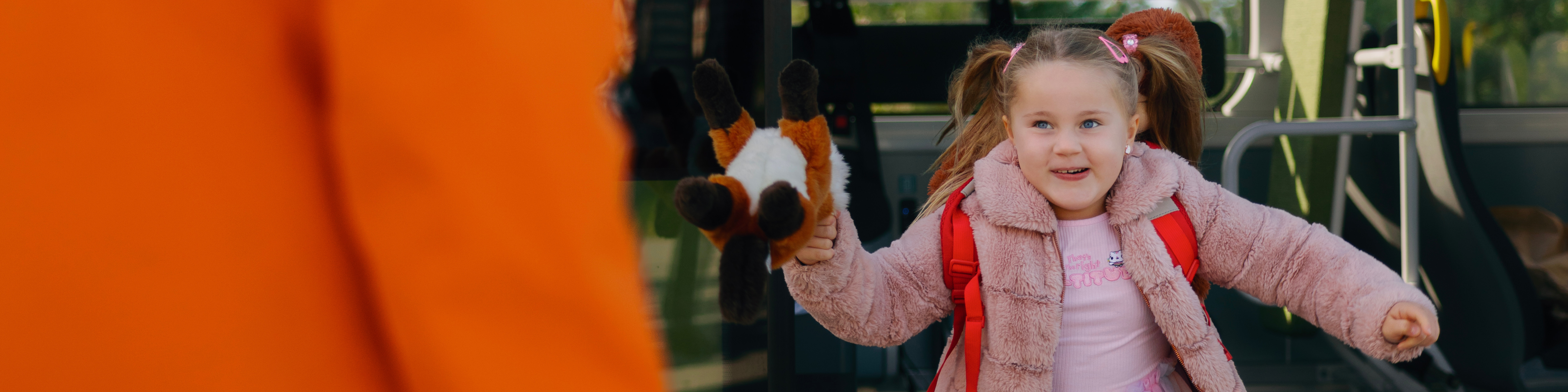 Liten tjej springer ut ur bussen. hon ler. Hon bär rosa kläder och har två tofsar på huvudet.