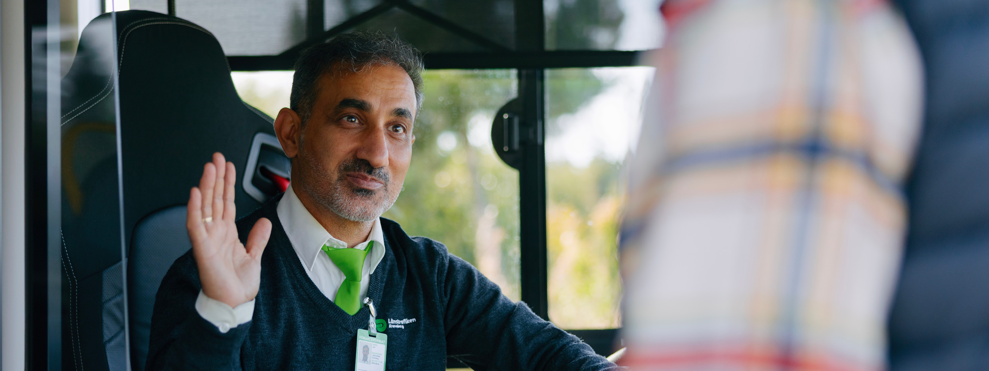 En manlig bussförare vinkar åt en resenär som går ombord på bussen.