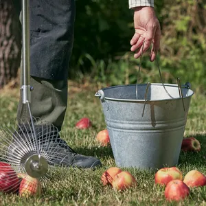 Metallkilen monteras på en metallhink med ena handen och håller i en äppelplockare med röda äpplen i den andra handen