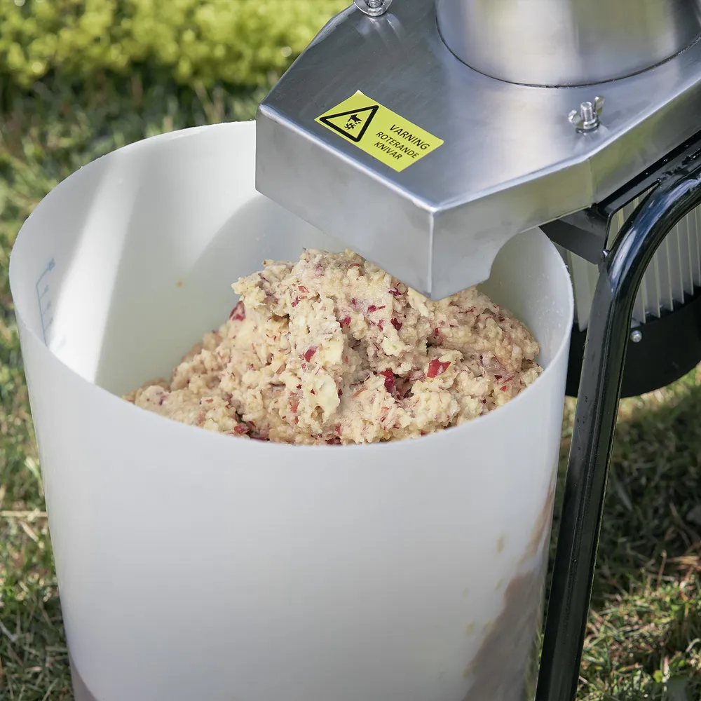 En fruktmassa bestående av krossade äpplen kommer ut från munstycket på en elektrisk fruktkross