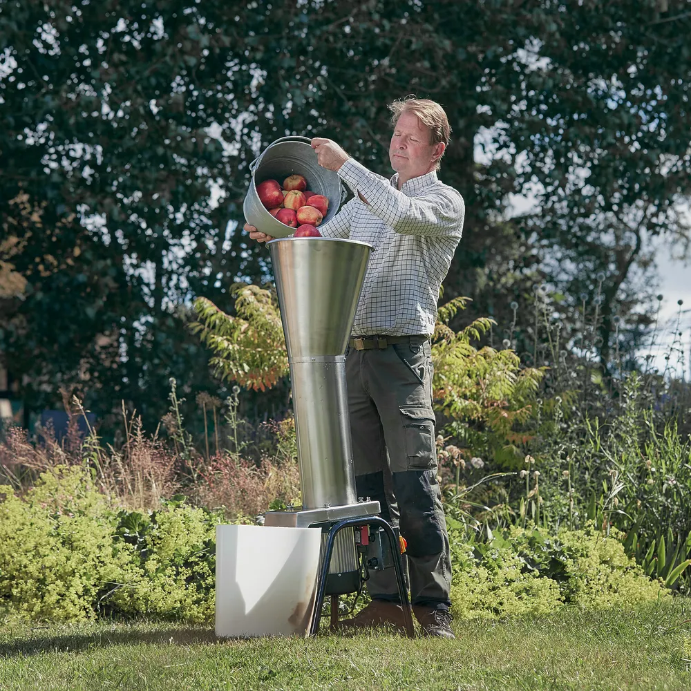 En vuxen man fyller en elektrisk fruktkross med röda äpplen utomhus på gräsmattan