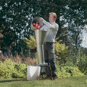 En vuxen man fyller en elektrisk fruktkross med röda äpplen utomhus på gräsmattan