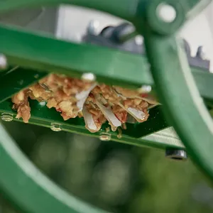 Krossade röda äpplen kommer ut från krossvalvarna i den manuella fruktkrossen från ett perspektiv underifrån