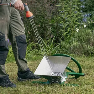 En vuxen man rengör en manuell fruktkross utomhus i trädgården med en vattenslang