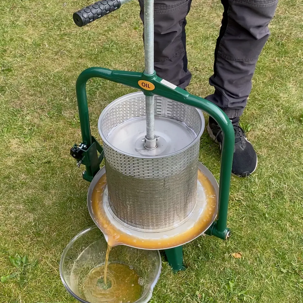 En vuxen man använder en cylinderformad fruktpress i rostfritt stål och gröna detaljer utomhus i trädgården