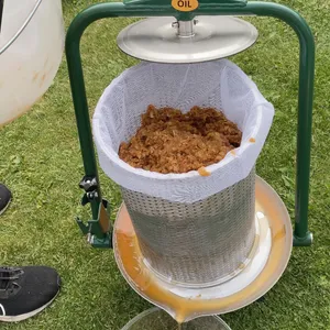 Krossad fruktmassa läggs i en öppen cylinderformad fruktpress i rostfritt stål med gröna detaljer