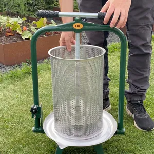 En vuxen man använder en cylinderformad fruktpress i rostfritt stål och gröna detaljer utomhus i trädgården