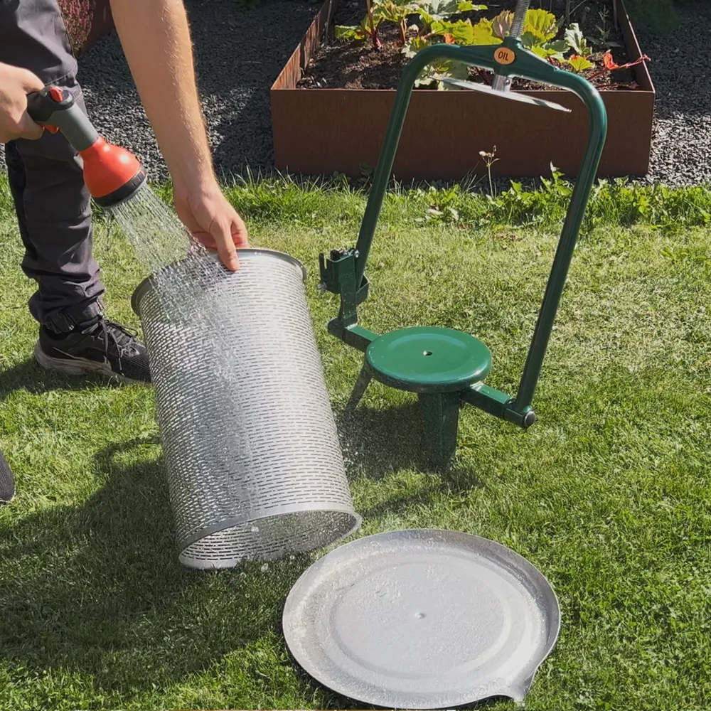 Rengjøring av en sylindrisk pressekurv med en vannslange ute på plenen