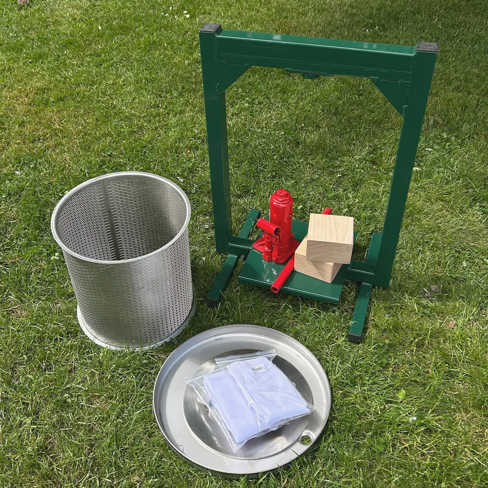 Hydraulisk fruktpress med tillhörande delar står utplacerade på en gräsmatta