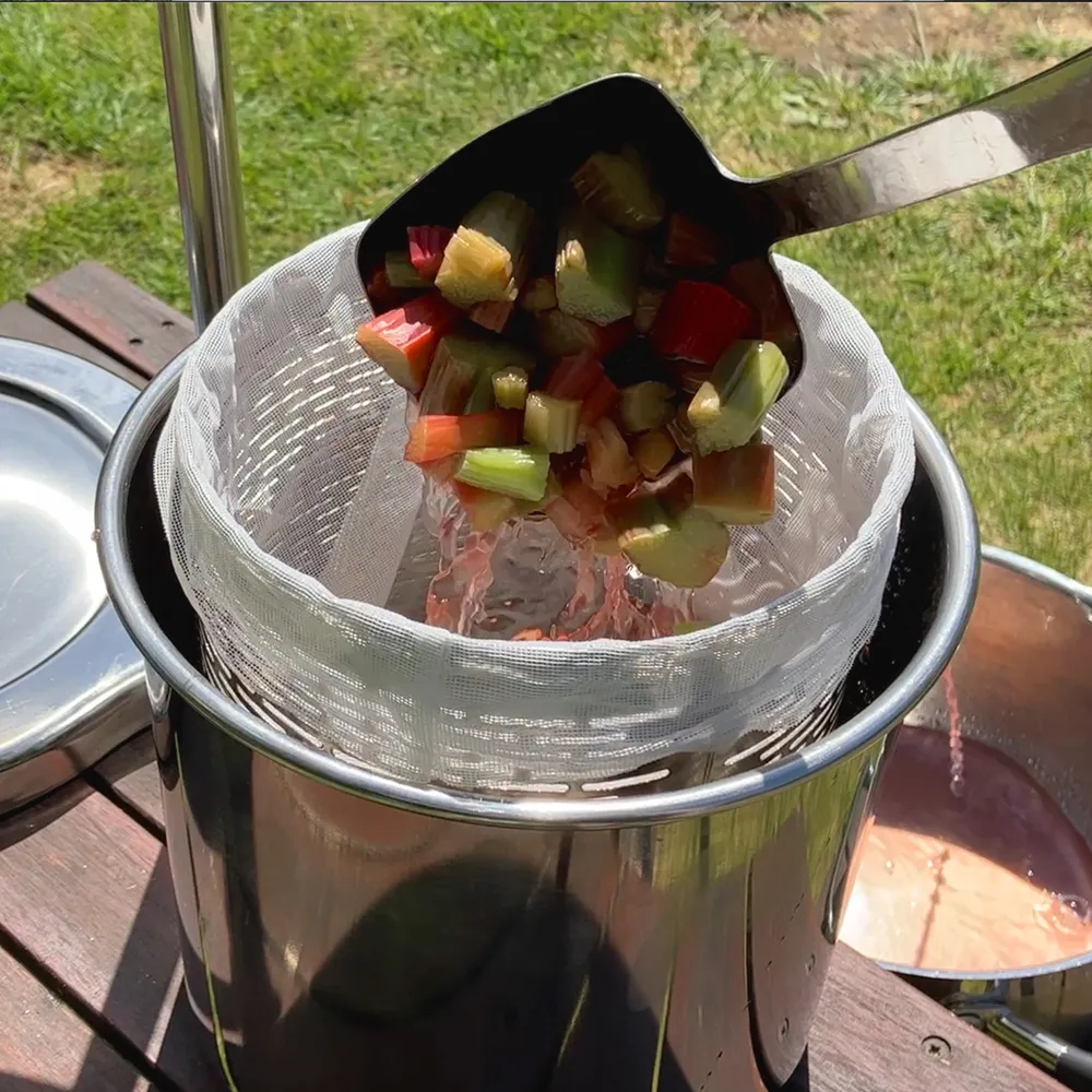 Tilhørende filterpose plassert i fruktpressens presskurv, fylt med rabarbra som skal presses til most