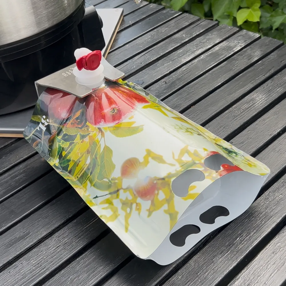 En rød og grønn stående pose fylt med juice plasseres i en BIB-holder for stabil fylling og forsegling