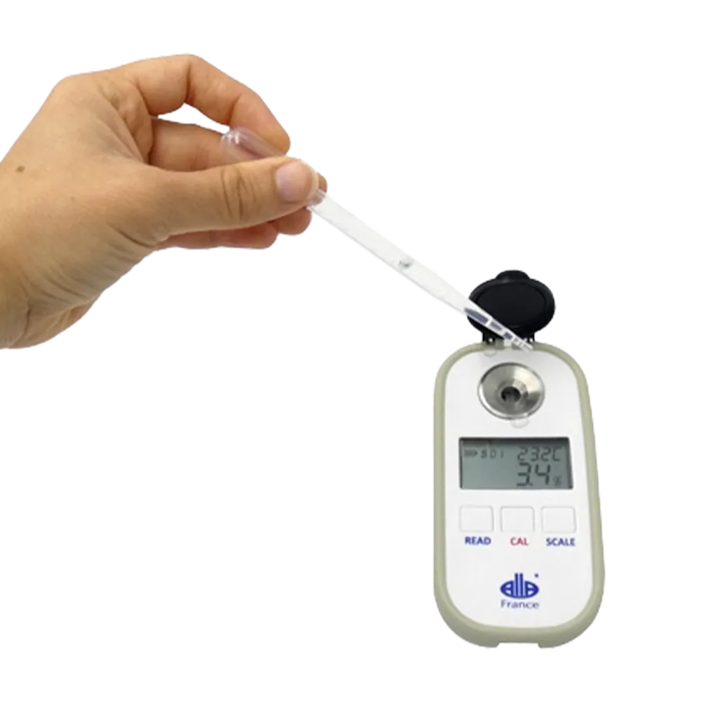 En hånd holder pipetten og slipper væske inn i refraktometeret