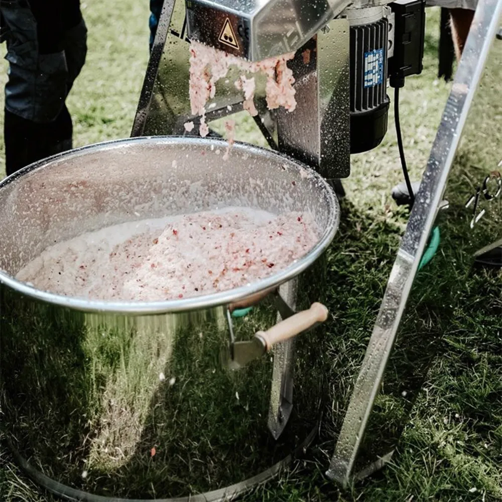 Kärl i rostfritt stål med krossade äpplen i som kommer från en elektrisk fruktkross