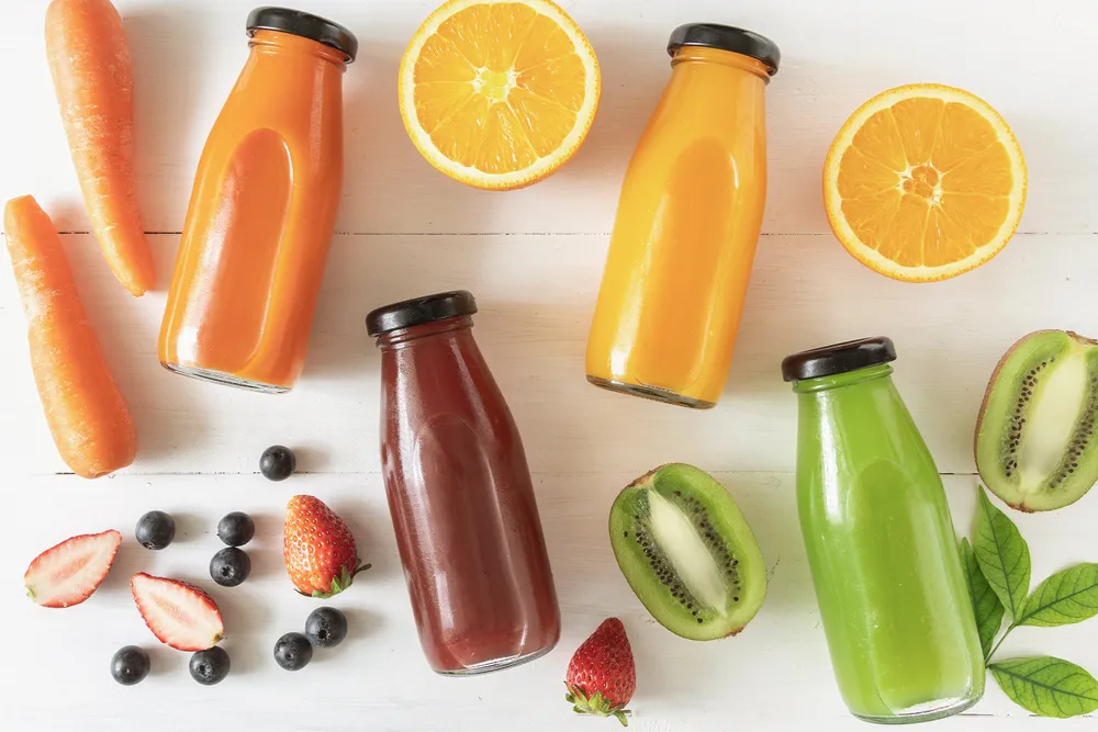 4 glassflasker med ulike juicer, en med gulrot, en med appelsin, en med bær og en med grønnsaker
