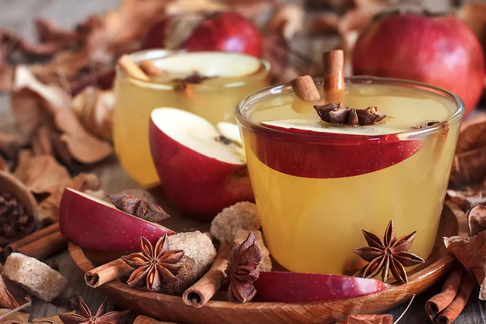 Et velfylt glass med gløgg med krydder og epler som dekorasjon i bakgrunnen
