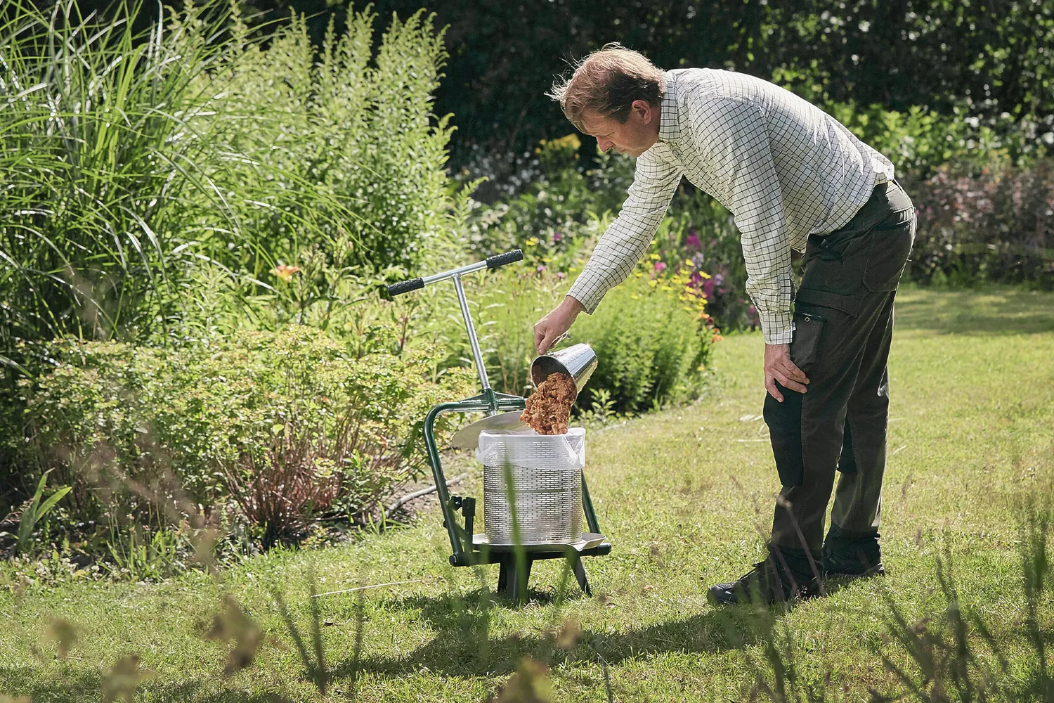 En mann i hagen som heller oppkuttede epler i en fruktpresse