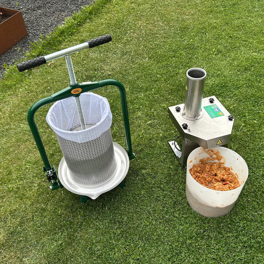 Original 18L -hedelmäpuristin seisoo vihreällä nurmikolla yhdessä Feedo-sähköhedelmämurskaimen kanssa