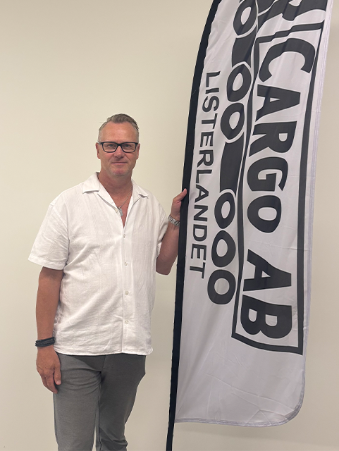 Foto på en man (Per Fälldin) som står vid en beach-flagga med MP Cargos logotype på.