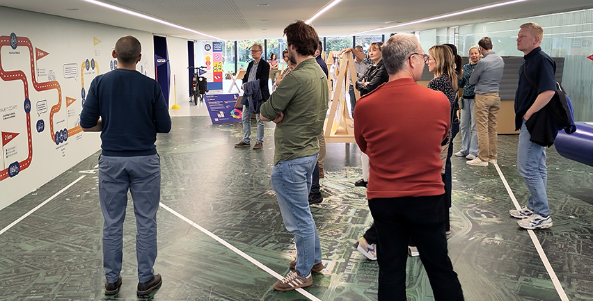 Människor i en hall med informationsskyltar, montrar med mera.