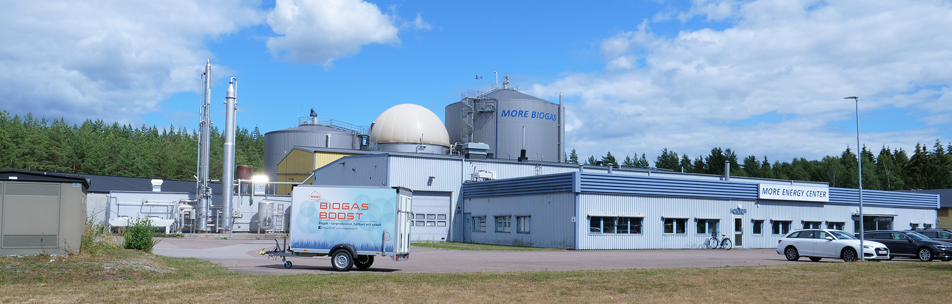 Foto på biogasanläggning mot en bakgrund av skog och blå himmel. 