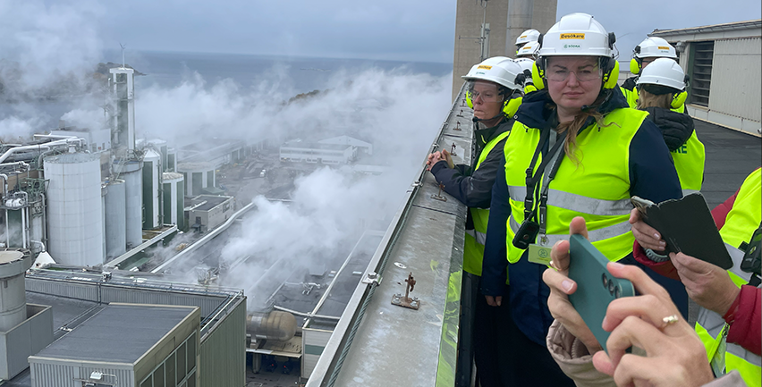 Människor i reflexvästar och skyddshjälmar på ett pappersbruk.