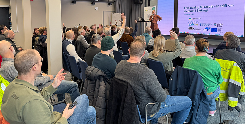 Sittande publik framför en kvinna som föreläser i en konferenssal. 