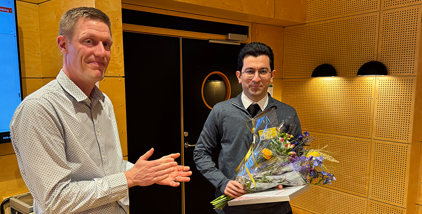 Foto på två män. Den ena håller i en blombukett och ett diplom.