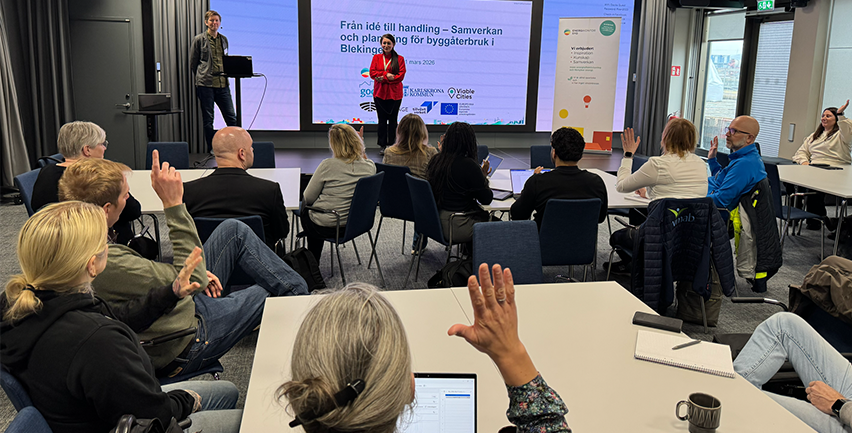 Människor i en föreläsningssal. Människor sträcker upp händerna i luften.