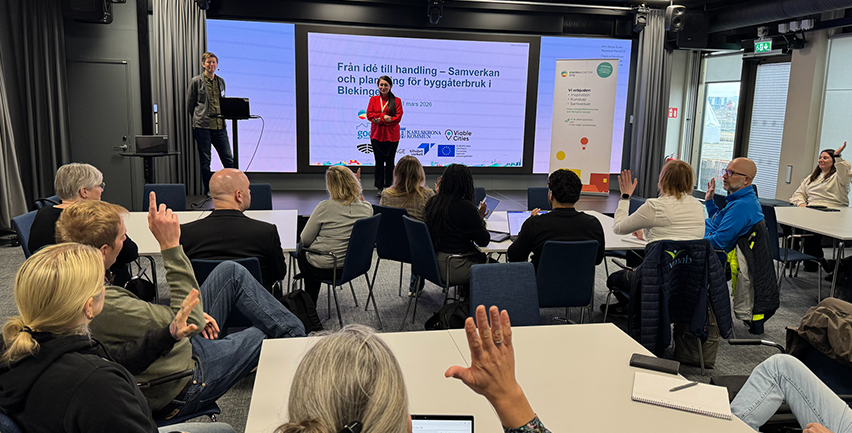 Sittande publik med händer i luften framför en scen med en man och en kvinna.