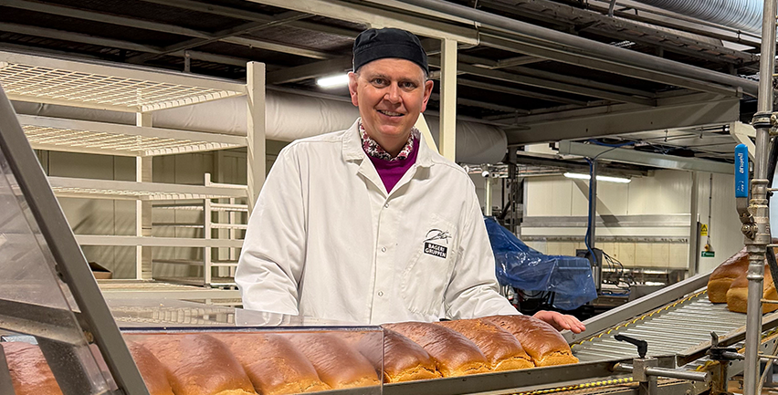 Man som står vid ett rullband med brödlimpor på.