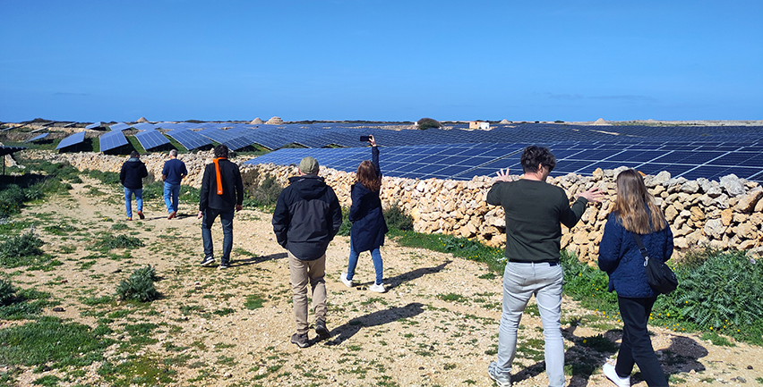 Solceller placerade mellan stenmurar. Blå himmel. Människor som promenerar.