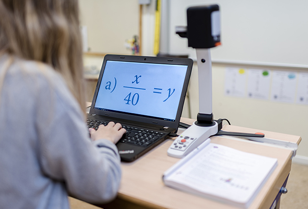 A girl in a classroom is using MagniLink PCViewer on a computer connected to the video magnifier MagniLink S Premium.