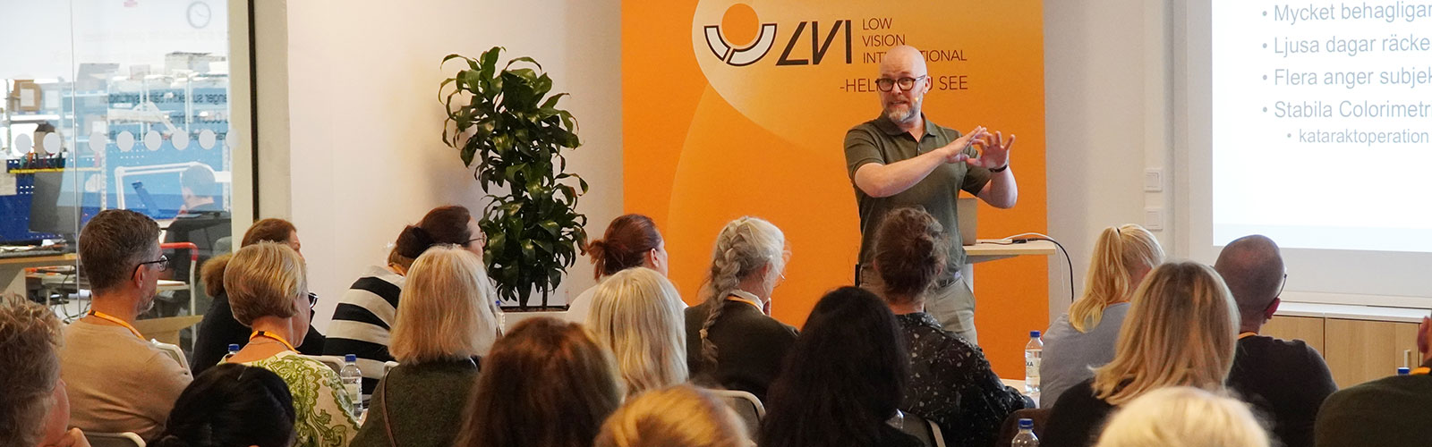 En man håller en föreläsning framför en stor skara deltagare i en konferenssal. I bakgrunden syns en orange rollup med LVIs logotyp.