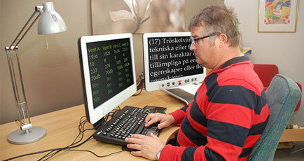Bild på en man som sitter och skriver på ett tangentbord och ser förstorad text på sin datorskärm.