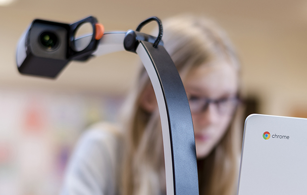 Bild där man ser i bakgrunden ser en elev som använder en Chromebook och en läskamera. I förgrunden syns baksidan av skärmen och avståndskameran.