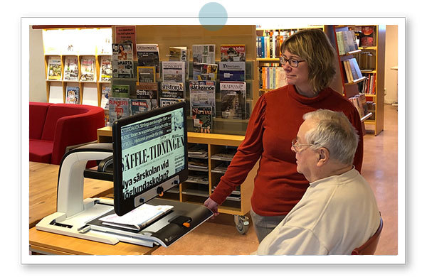 Pensionären Åke läser tidningen på ett bibliotek med hjälp av en läskamera.