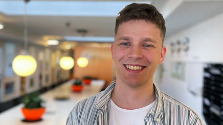 En leende Max med randig skjorta står framför LVIs långa bord.