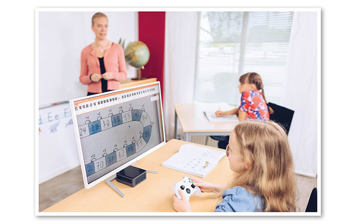 Bild i ett klassrum där eleven har en kontroll- och styrenhet som överför bilden från den takmonterade kameran till en tillkopplad monitor.