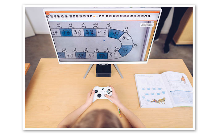 Bild in einem Klassenzimmer, in dem der Schüler über ein Kontroll- under Steuergerät verfügt, die das Bild von der deckenmontierten Kamera auf einen angeschlossenen Monitor überträgt.