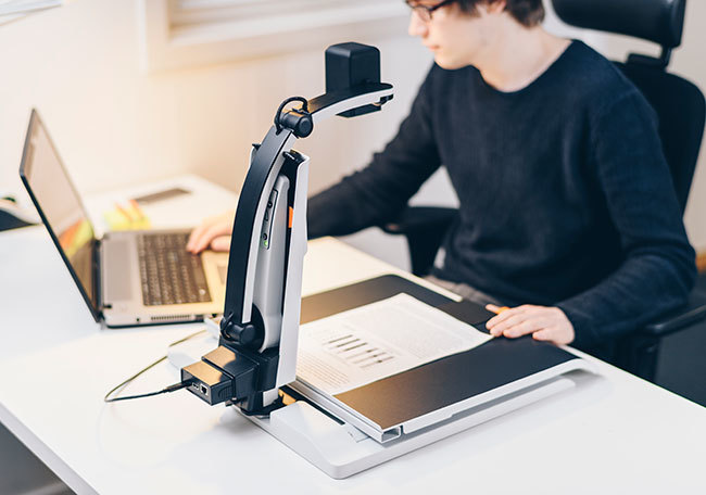 Ein Mann sitzt und arbeitet an einem Computer, der an einen MagniLink S Premium 2 mit Dockingstation angeschlossen ist.