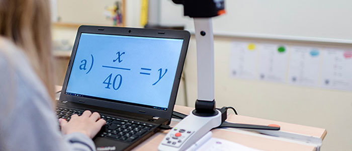 A girl in a class room uses a MagniLink S video magnifier connected to a computer with the software MagniLink PCViewer to see whats in a math book.