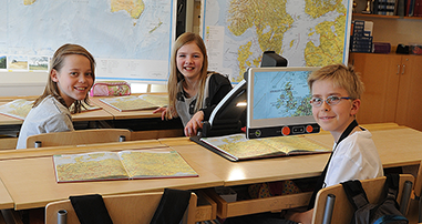 Bild von drei Schülern in einem Klassenzimmer, in dem einer von ihnen einen MagniLink Zip verwendet, um die Karte in einem Kartenbuch anzuzeigen.